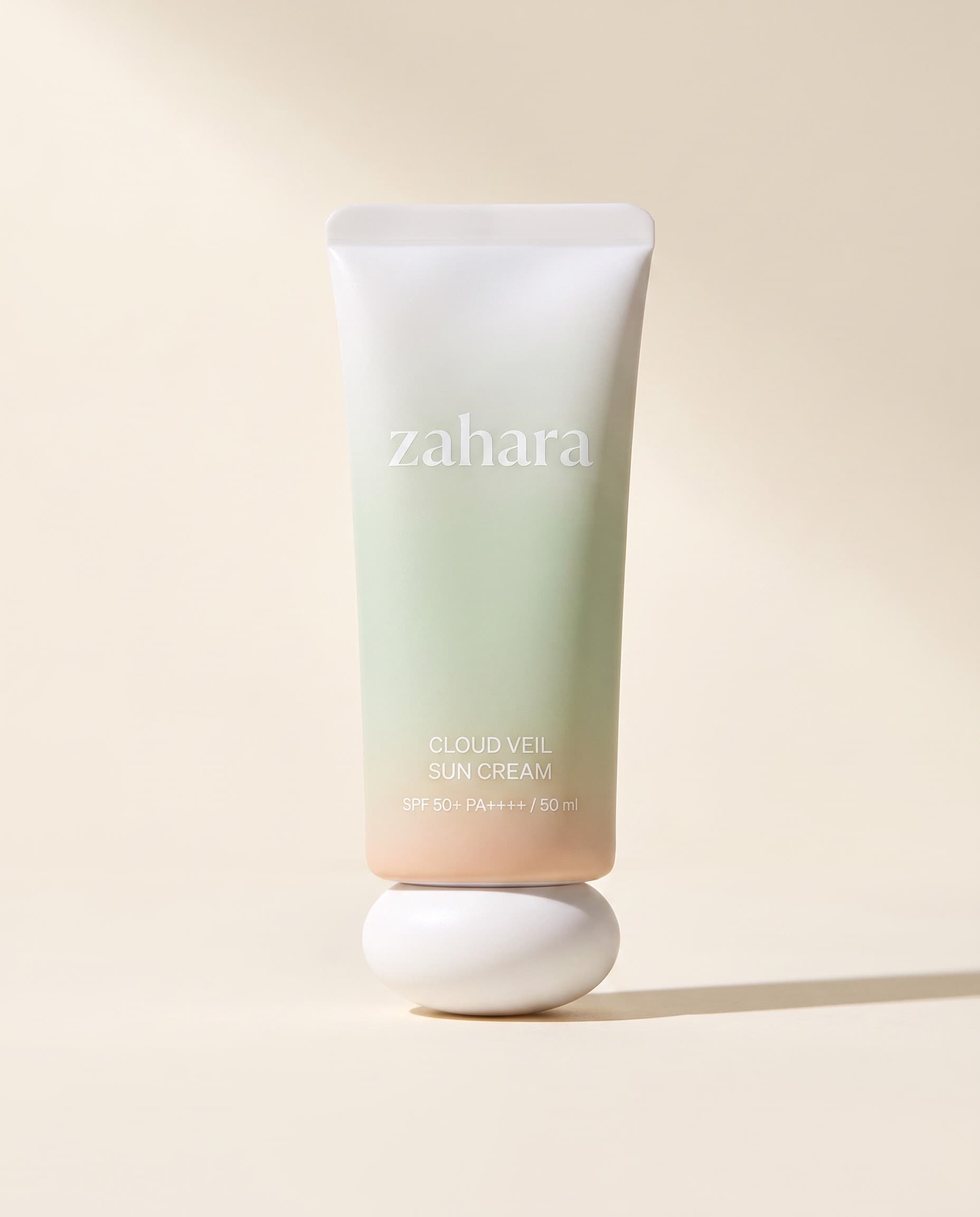 Zahara Cloud Veil Sun Cream packshot: a porcelain-to-pale-celadon tube with a sculptural white cap.