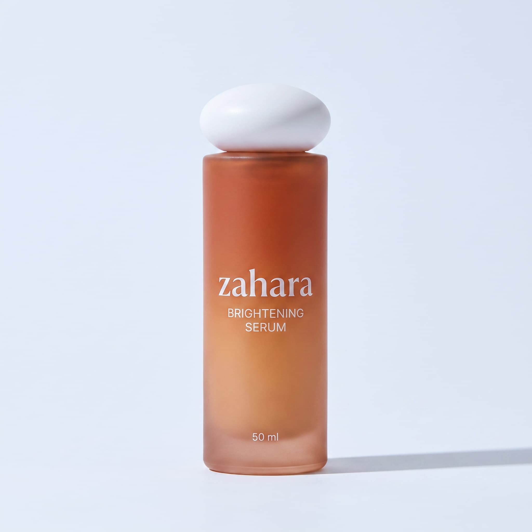 Zahara Brightening Serum packshot: amber-to-terracotta gradient bottle with the white pebble cap.
